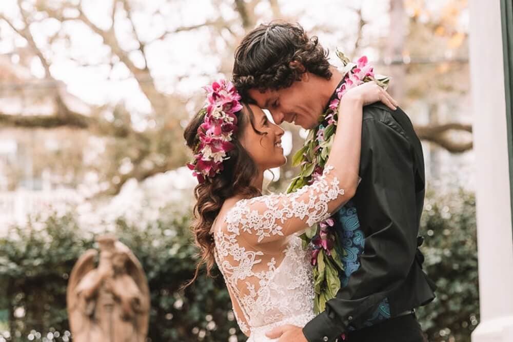 A joyful couple embraces, adorned with floral crowns, amidst a romantic outdoor setting.