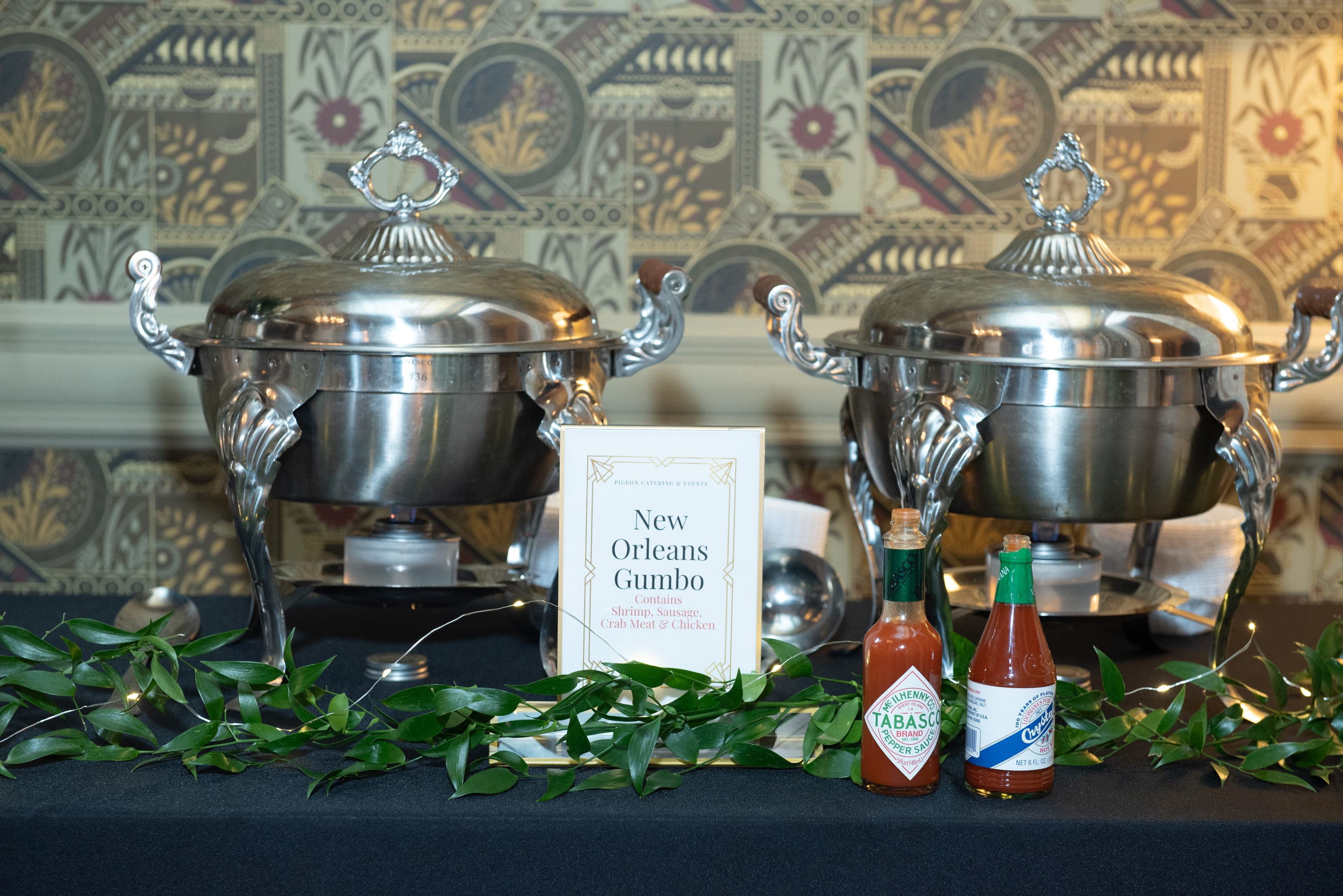 Two silver chafing dishes labeled "New Orleans Gumbo" with Tabasco and Crystal hot sauces on a decorated table.