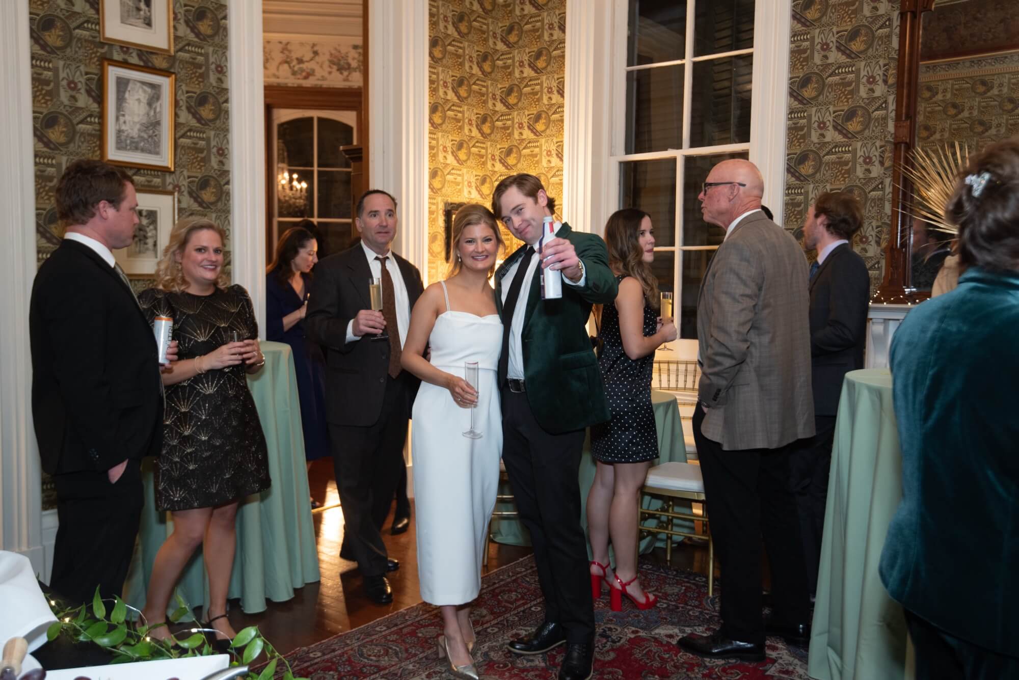 A group of elegantly dressed people socialize at a formal event in a beautifully decorated room.
