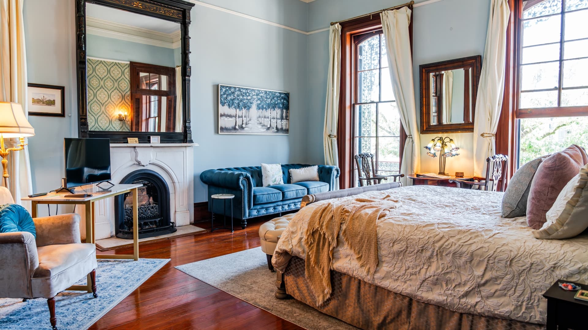 A beautifully designed bedroom with a large bed, elegant furnishings, and natural light streaming through tall windows.