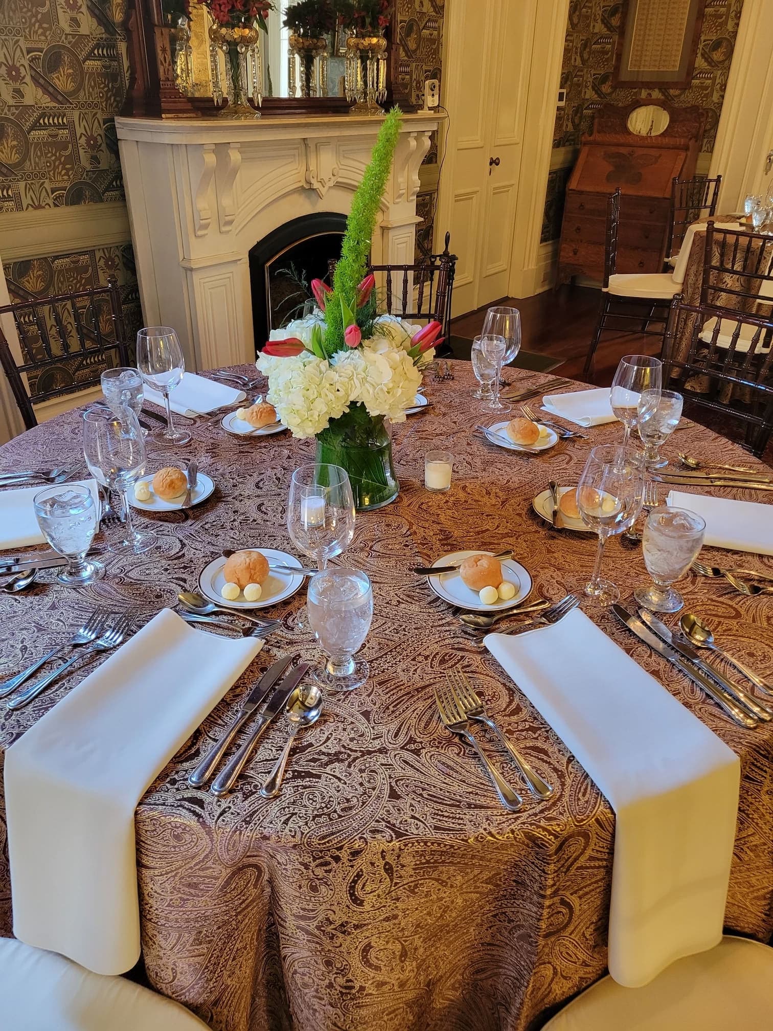 A beautifully set dining table with elegant tableware, bread rolls, and a floral centerpiece.