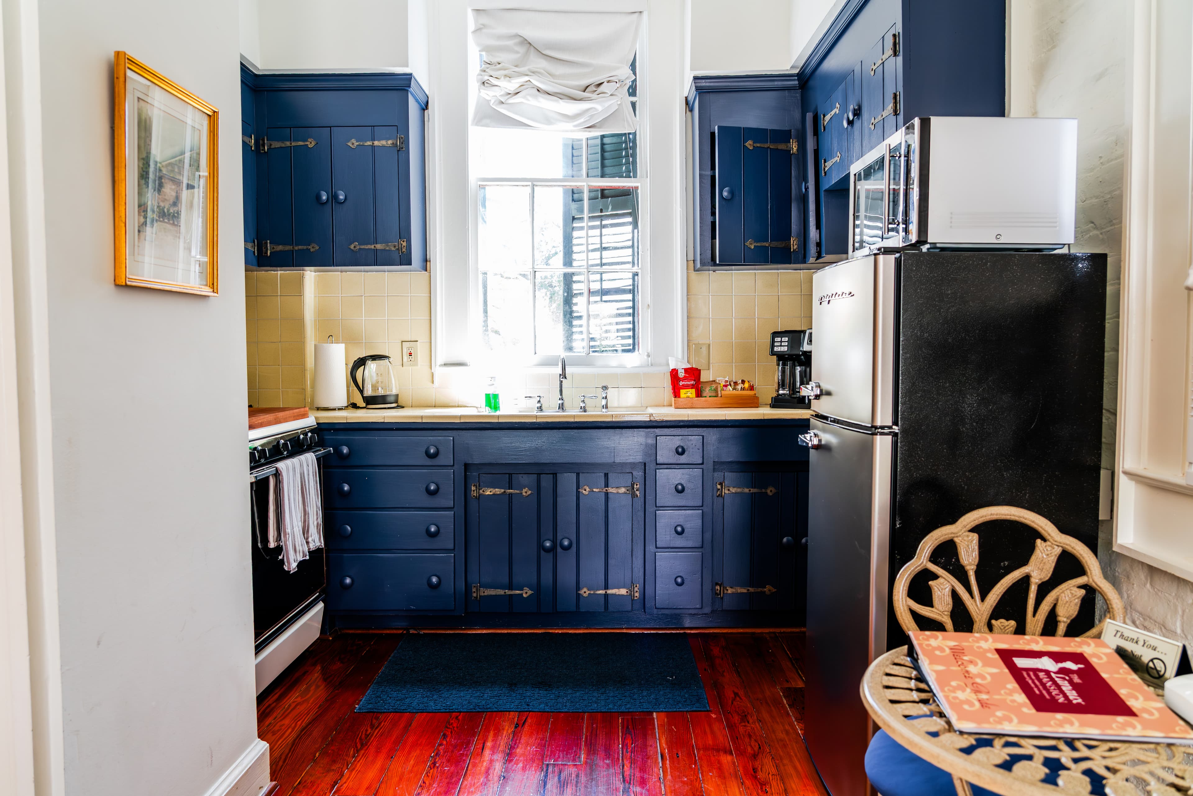 Bright kitchen with dark blue cabinets, a stainless steel fridge, and wooden floors.