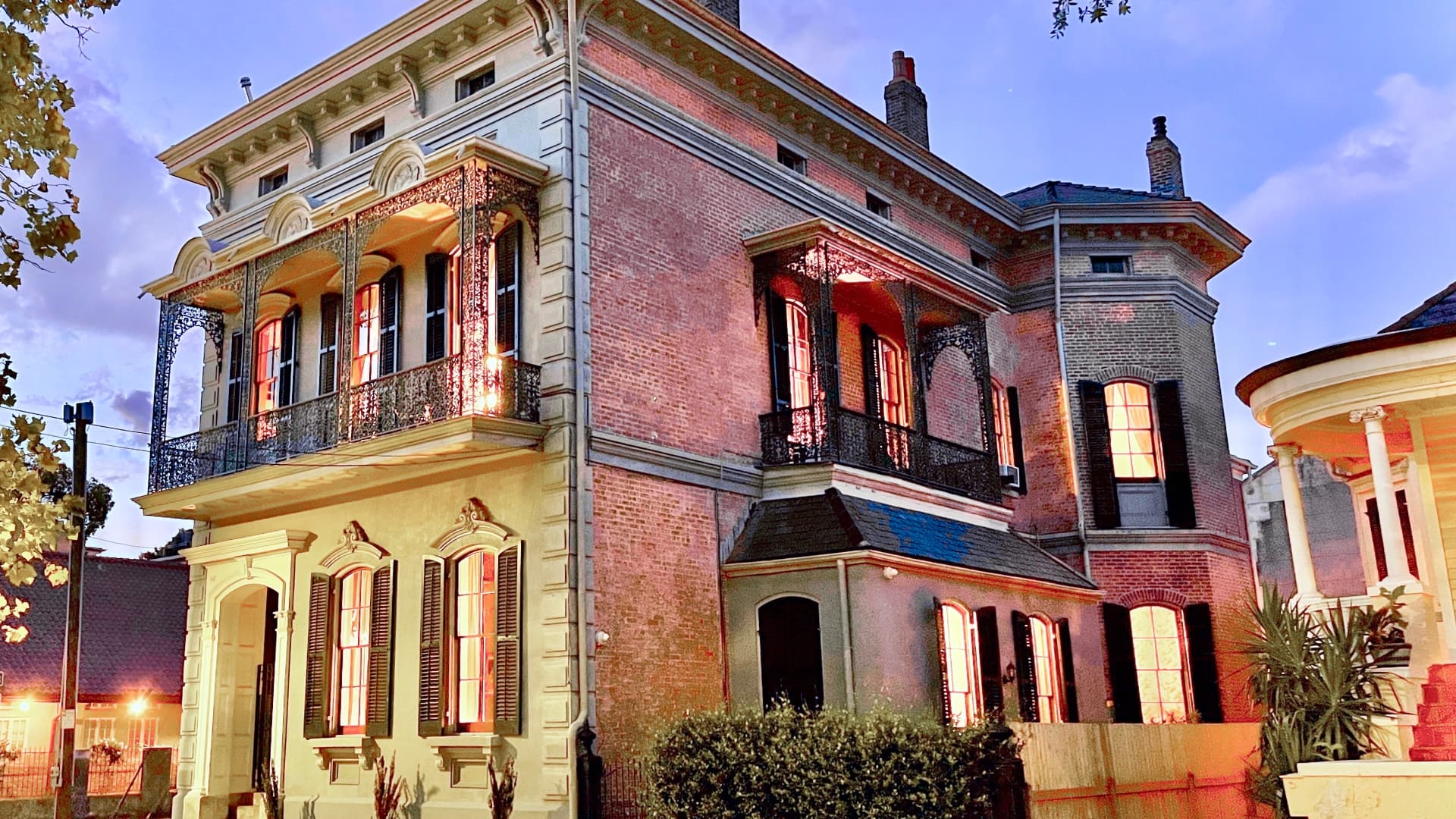 Historic brick mansion with intricate balconies, illuminated at dusk.