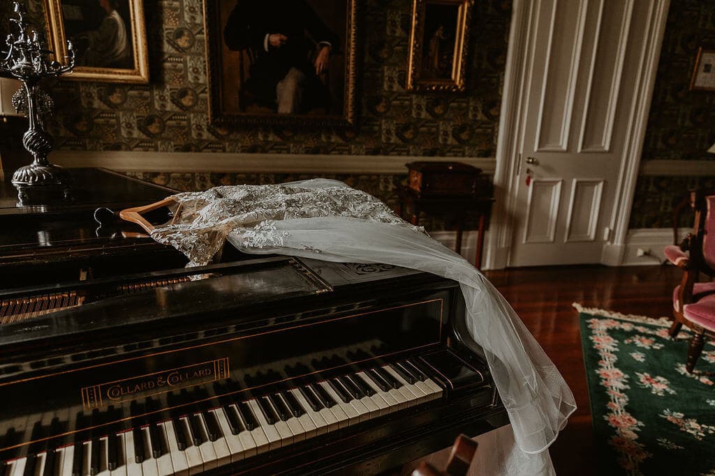 A wedding dress hangs elegantly on a piano in a richly decorated room.