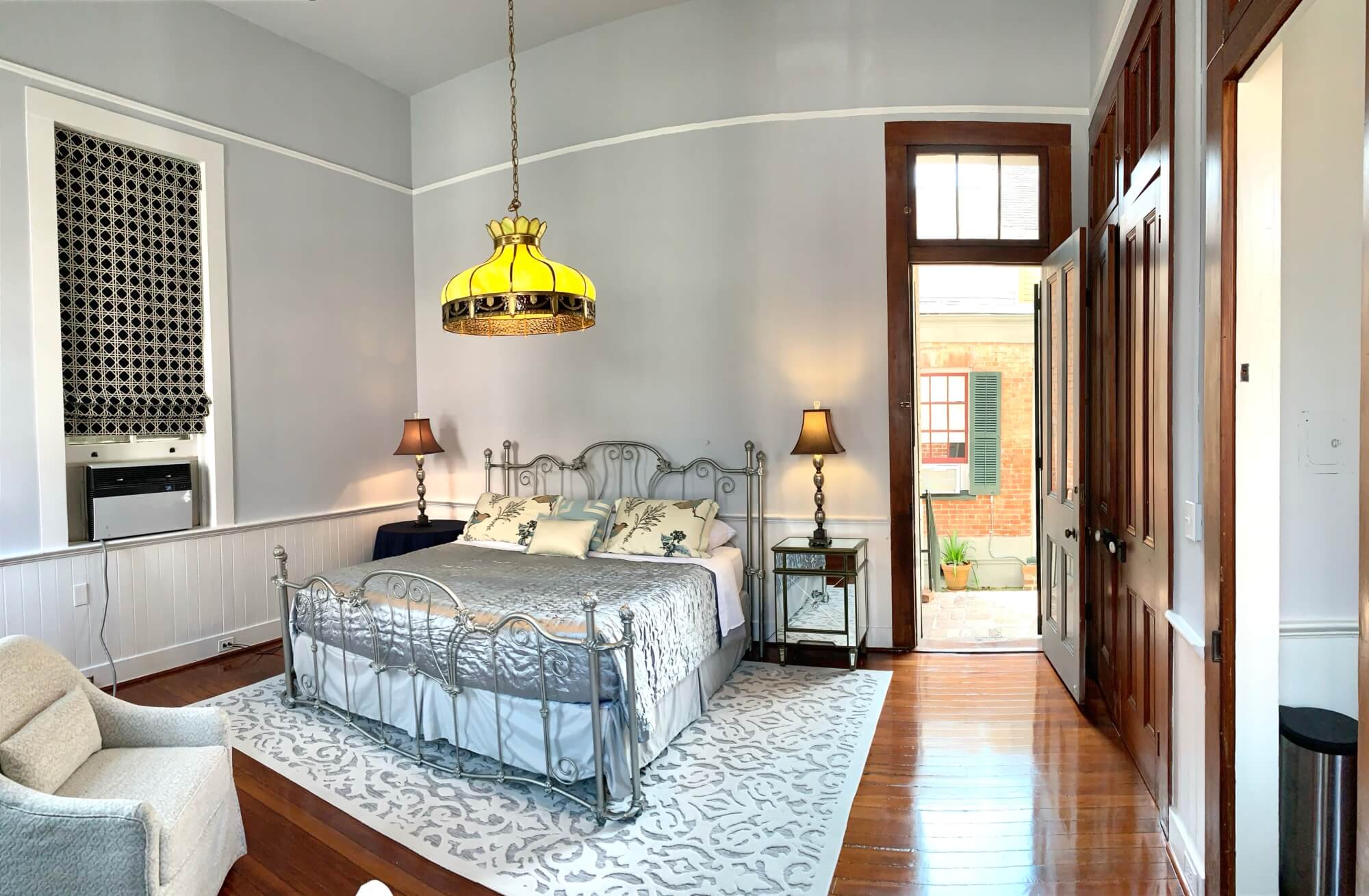 A cozy bedroom featuring a metal-framed bed, warm lighting, and an open door leading to an outdoor area.