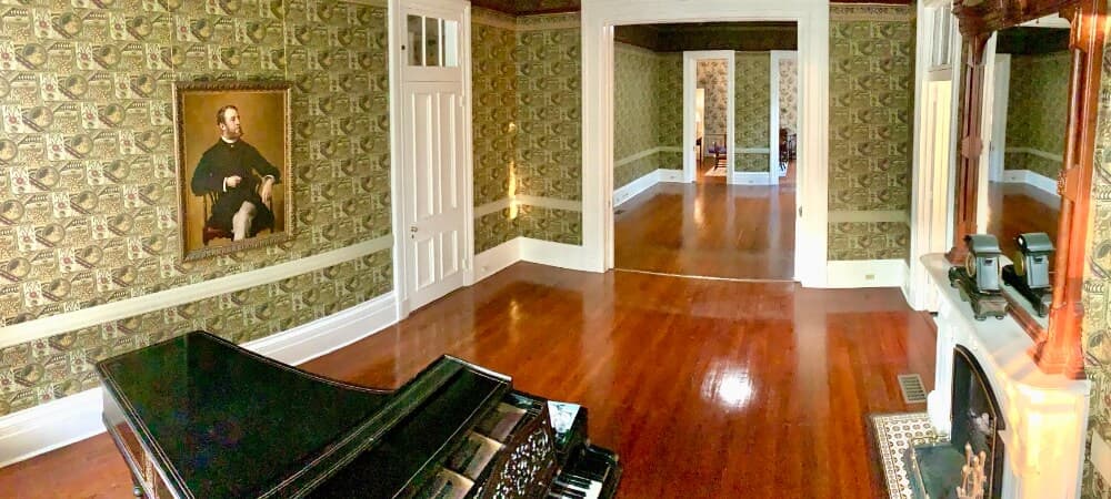 A spacious room featuring a grand piano, adorned with vintage wallpaper and a portrait on the wall.