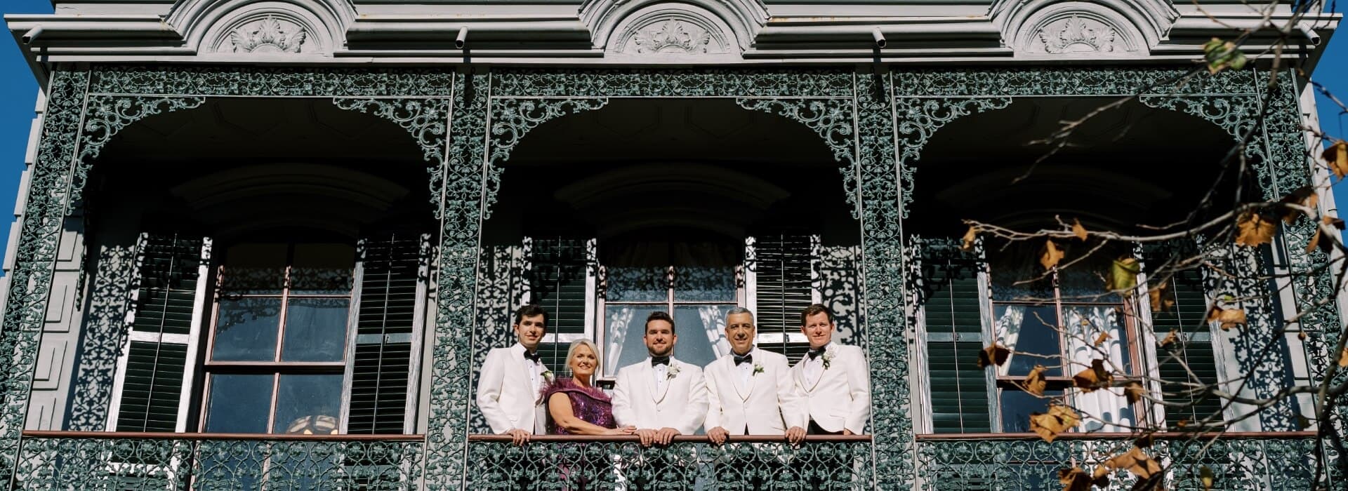 A group of five people in formal attire poses on a decorative balcony.