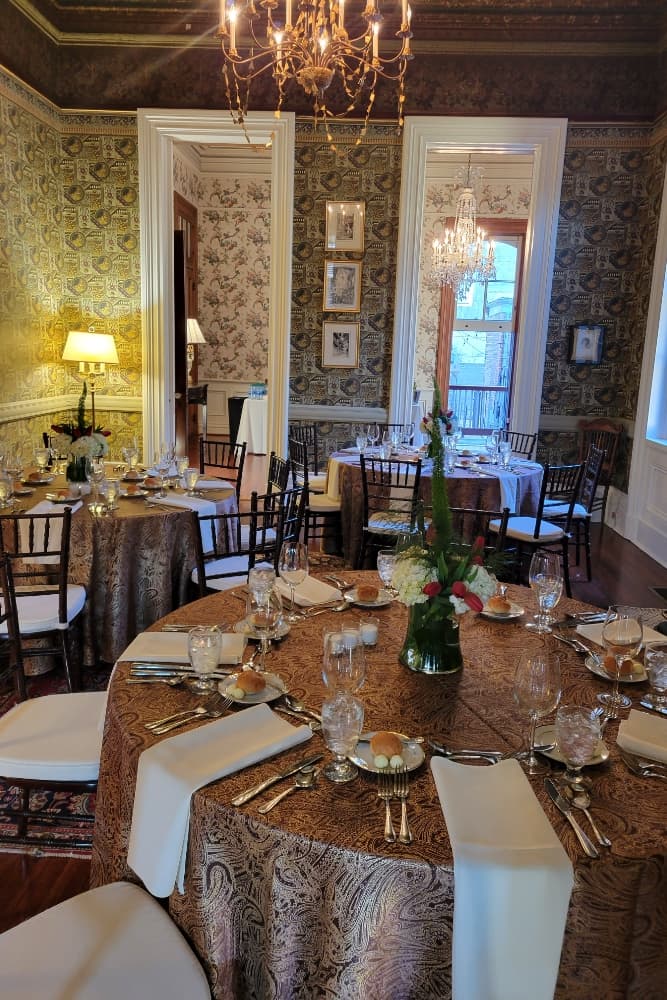 A beautifully arranged dining room featuring elegant tables, intricate wallpaper, and sparkling chandeliers.