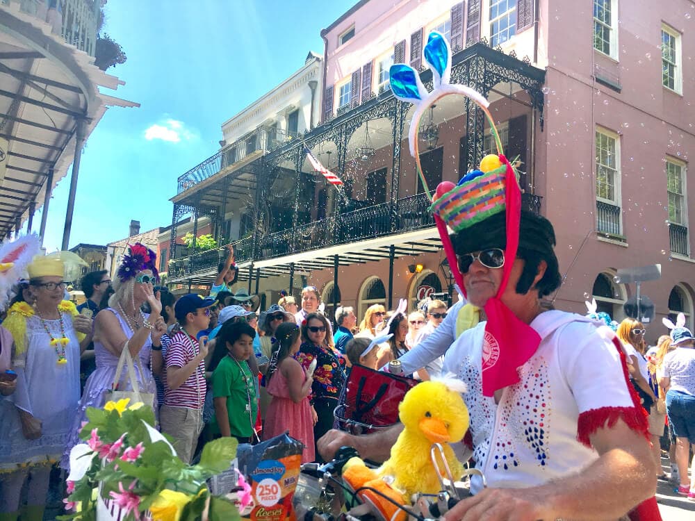 A festive crowd gathers on a sunny street, celebrating with colorful costumes and decorations.
