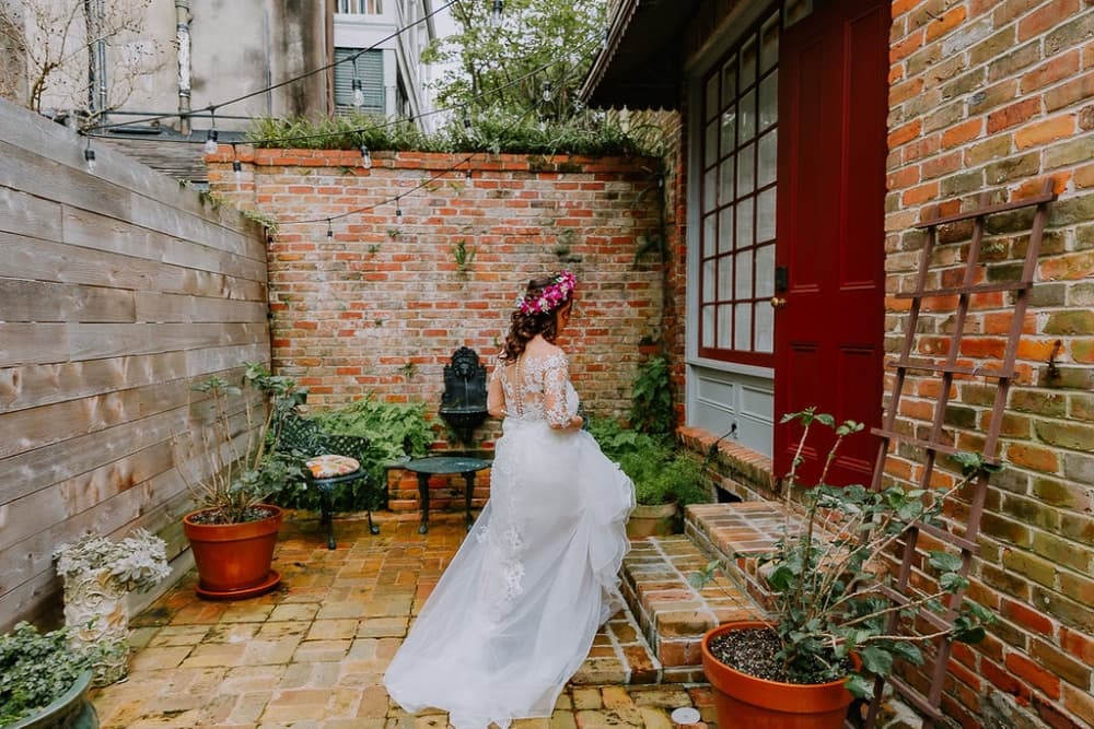 A bride in a white gown walks toward a red door in a brick-walled garden.