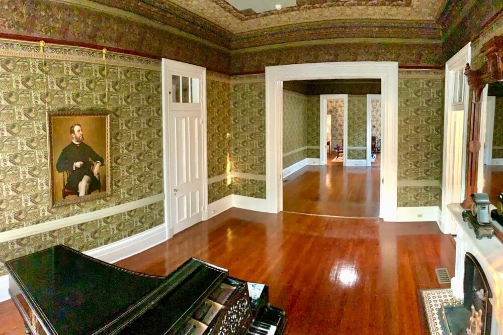 A grand room featuring a piano, ornate wallpaper, and a portrait on the wall.