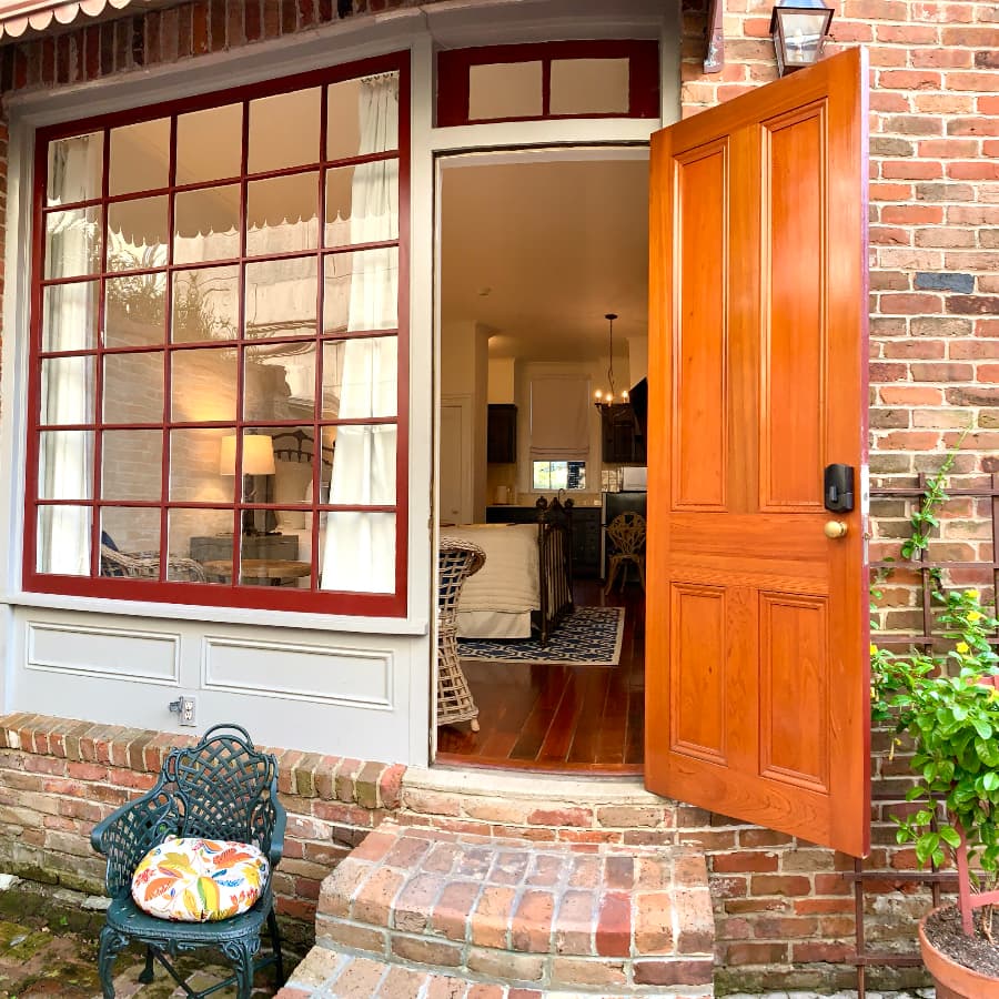 An open wooden door reveals a cozy interior with brick walls and a glimpse of a stylish chair and decor.