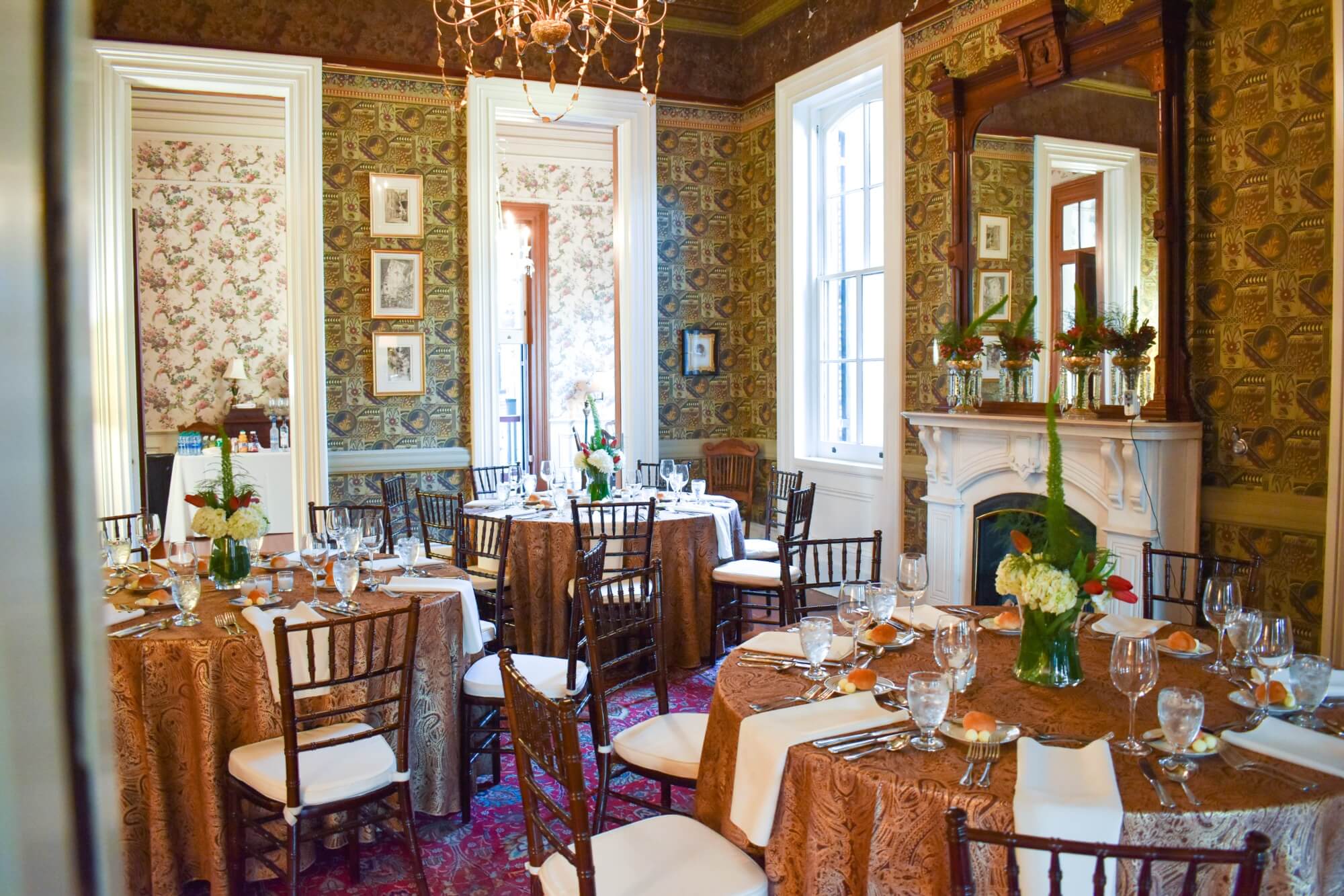 Elegant dining room with ornate wallpaper, flower centerpieces, and set tables.