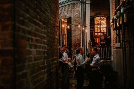 A dimly lit alleyway with people socializing amid brick walls and string lights.