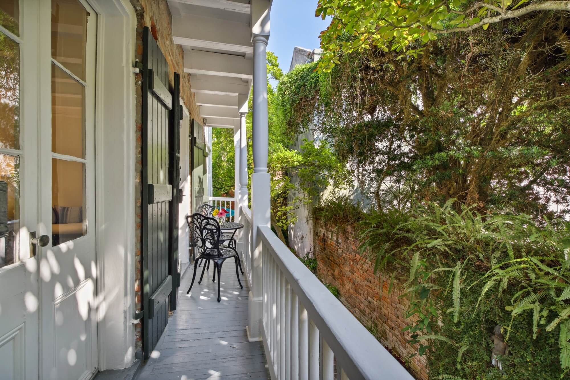 A sunny balcony overlooks lush greenery with chairs for seating.