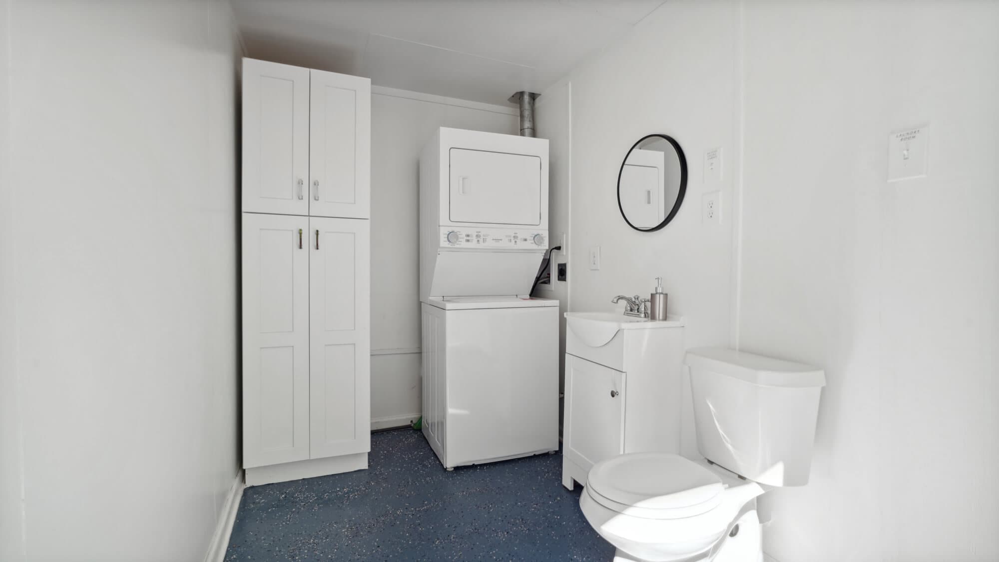 A clean, white laundry room featuring a stacked washer and dryer, a sink, and a toilet.