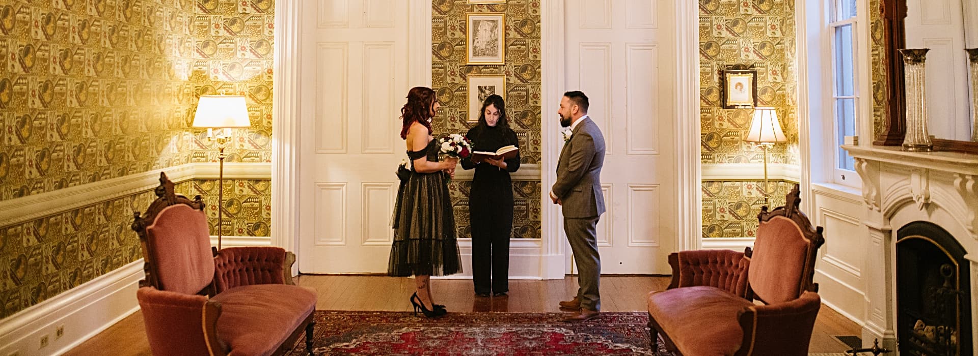 A couple stands in an elegantly decorated room while exchanging vows with an officiant.