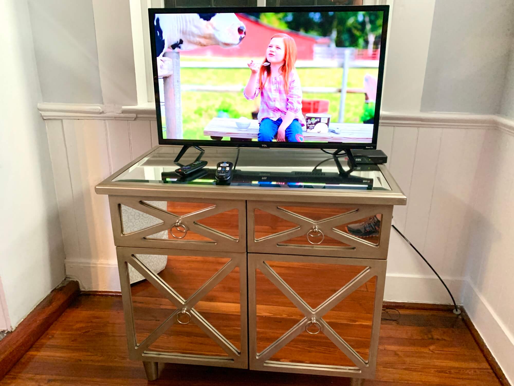A stylish mirrored TV stand with a television displaying a girl interacting with a cow outdoors.
