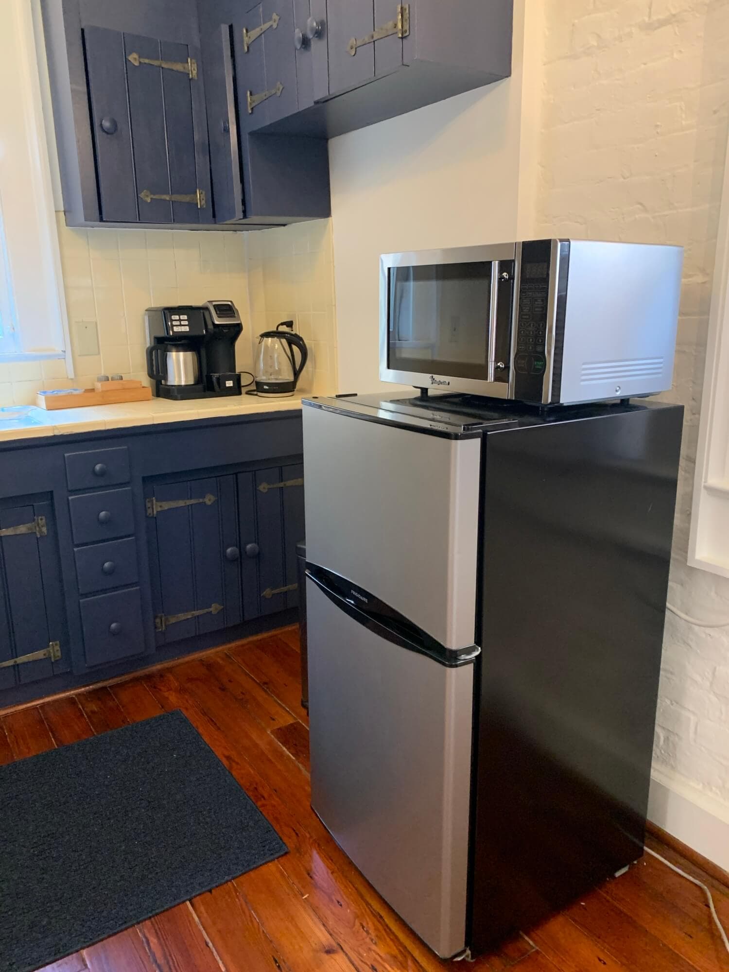 A kitchen corner featuring a silver and black refrigerator with a microwave on top, alongside a coffee maker and kettle.