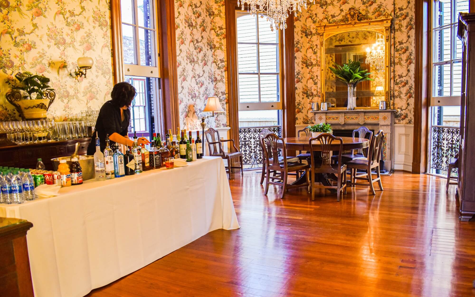 An elegantly decorated room featuring a bar setup and a dining table, with a person arranging drinks.