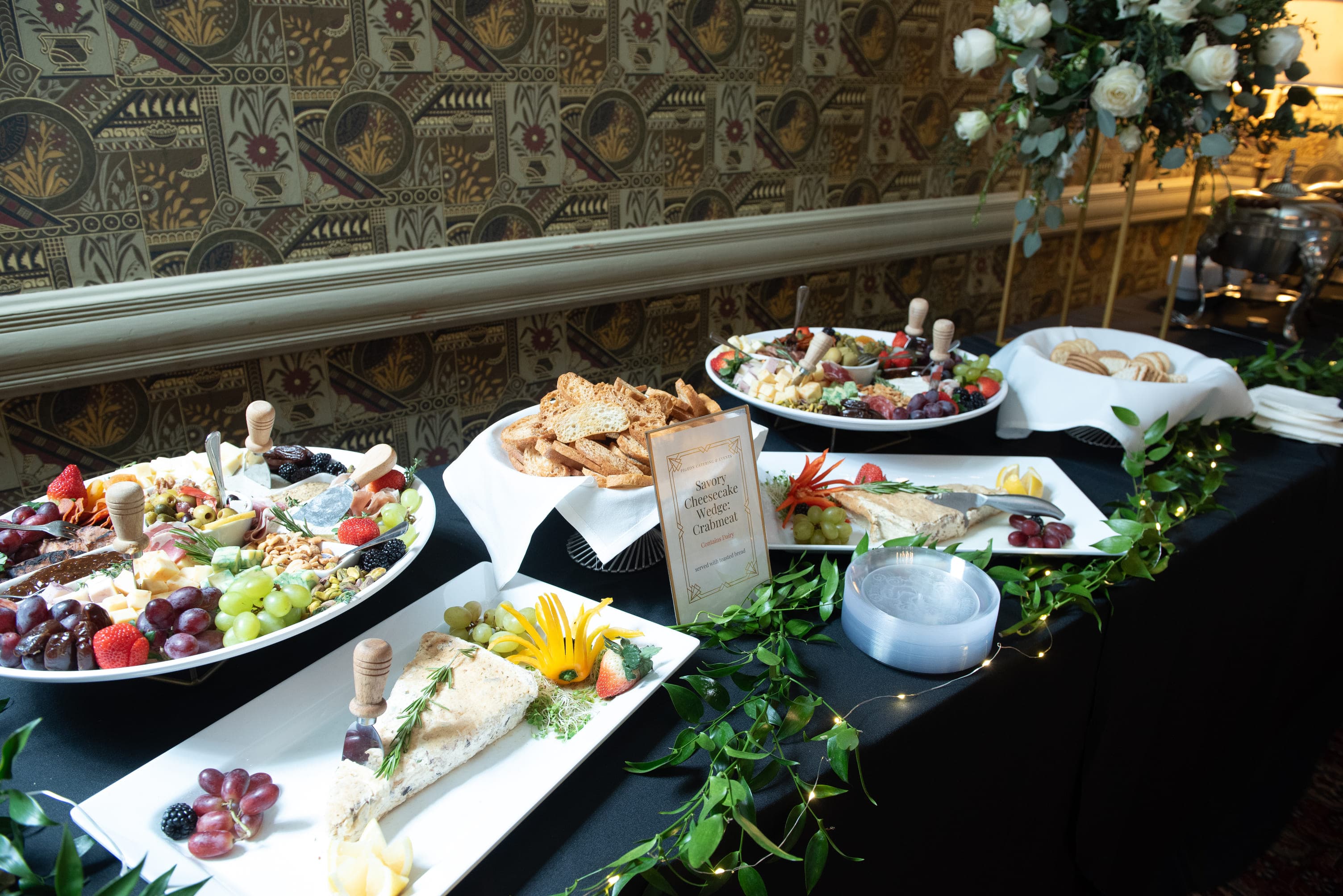 A buffet table featuring an assortment of cheeses, fruits, nuts, and crackers, set against an elegant backdrop.