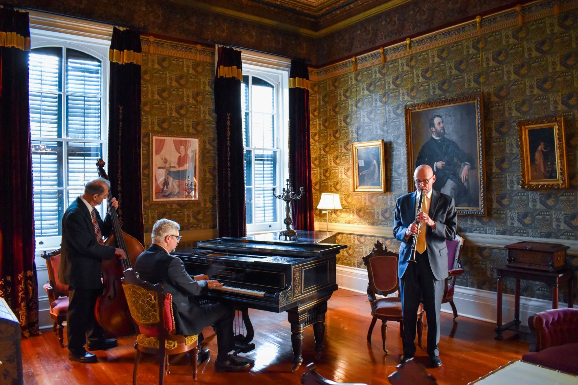 Three musicians play instruments in a richly decorated room with antique furnishings.