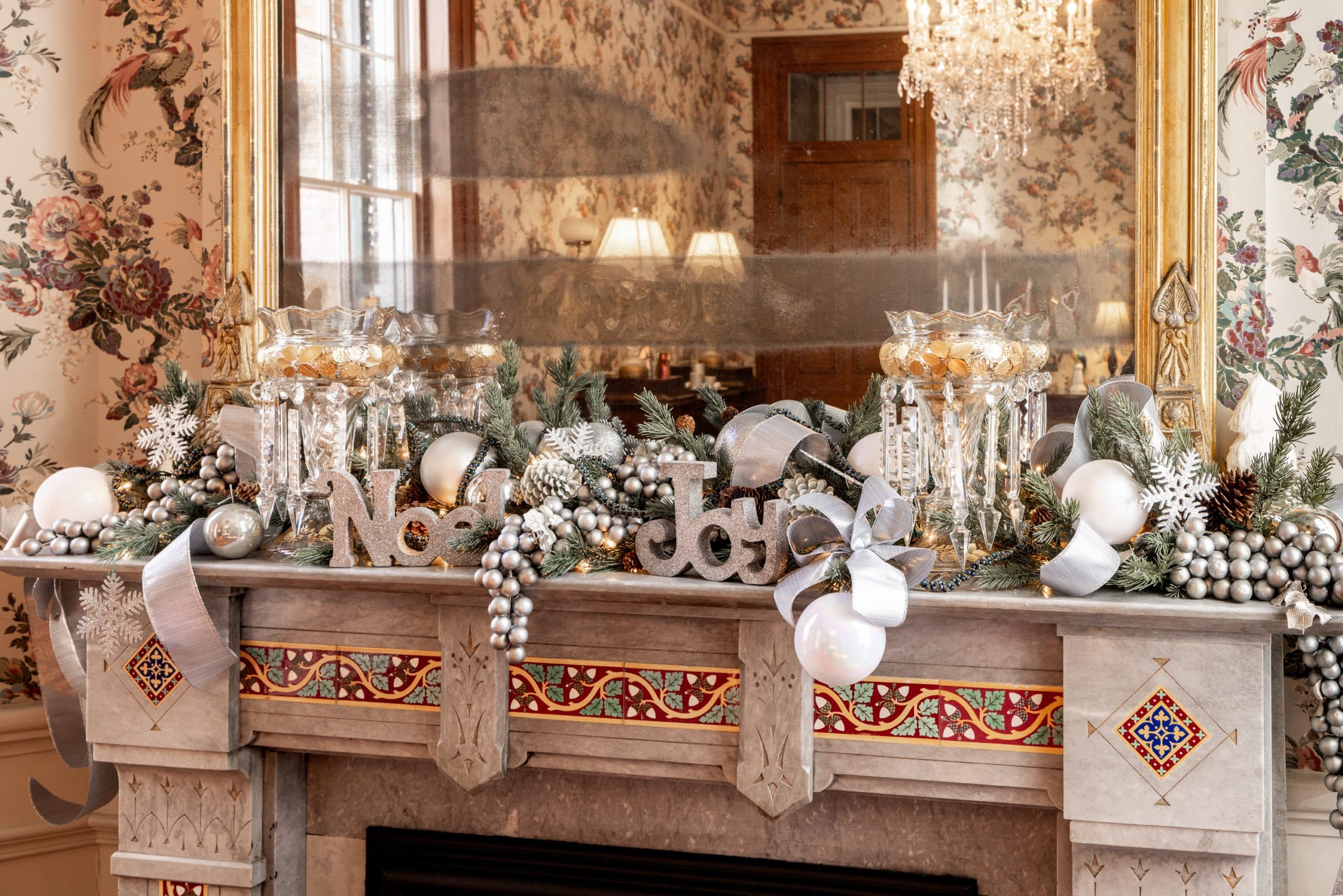 A beautifully decorated fireplace mantel featuring "Noel" and "Joy" signs, adorned with festive greenery and ornaments. A beautifully decorated fireplace mantel featuring "Noel" and "Joy" signs, adorned with festive greenery and ornaments.