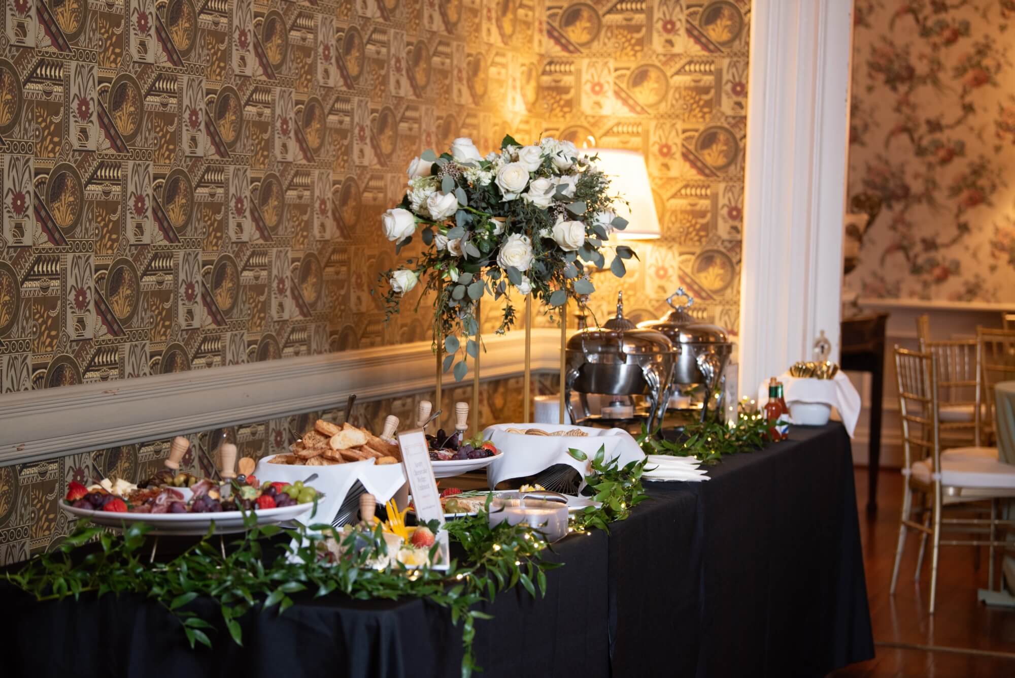 A buffet table adorned with floral arrangements and various dishes set against a decorative wallpaper backdrop.